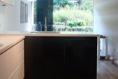 Cette photo montre une cuisine ouverte moderne en L de taille moyenne avec un évier 1 bac, un placard à porte plane, des portes de placard noires, plan de travail en marbre, un électroménager noir, un sol en ardoise, une péninsule, un sol gris et un plan de travail blanc.