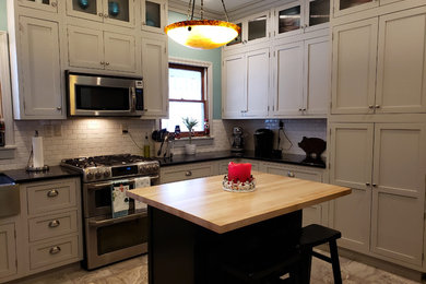 Inspiration for a large transitional u-shaped ceramic tile and beige floor kitchen pantry remodel in Other with a farmhouse sink, recessed-panel cabinets, white cabinets, quartz countertops, white backsplash, ceramic backsplash, stainless steel appliances, an island and black countertops