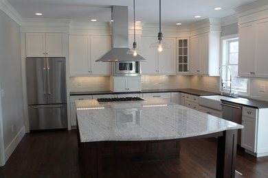 Example of a trendy l-shaped dark wood floor kitchen design in New York with a farmhouse sink, shaker cabinets, white cabinets, granite countertops, white backsplash, subway tile backsplash, stainless steel appliances and an island