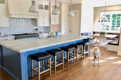 Example of a large country single-wall medium tone wood floor and brown floor eat-in kitchen design in Orange County with shaker cabinets, white cabinets, granite countertops, white backsplash, porcelain backsplash, colored appliances, an island, white countertops and a farmhouse sink