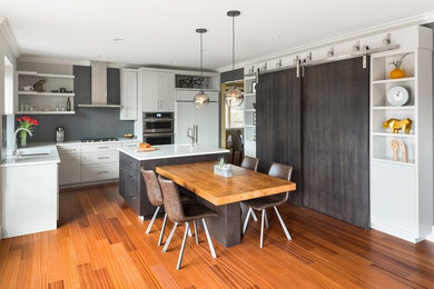 Inspiration for a transitional l-shaped medium tone wood floor kitchen remodel in Vancouver with an undermount sink, shaker cabinets, white cabinets, gray backsplash, paneled appliances and two islands