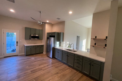 Example of a mid-sized beach style ceramic tile, brown floor and vaulted ceiling enclosed kitchen design in Phoenix with an undermount sink, recessed-panel cabinets, green cabinets, quartz countertops, stainless steel appliances and white countertops