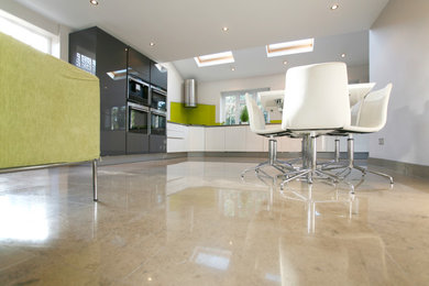 Inspiration for a medium sized contemporary l-shaped kitchen/diner in Hertfordshire with an integrated sink, flat-panel cabinets, white cabinets, engineered stone countertops, green splashback, glass tiled splashback, black appliances, limestone flooring, grey floors, grey worktops, a drop ceiling and a feature wall.