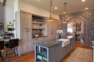 Large farmhouse galley medium tone wood floor and brown floor eat-in kitchen photo in Atlanta with a farmhouse sink, paneled appliances, an island, shaker cabinets, light wood cabinets, soapstone countertops, brown backsplash and stone slab backsplash