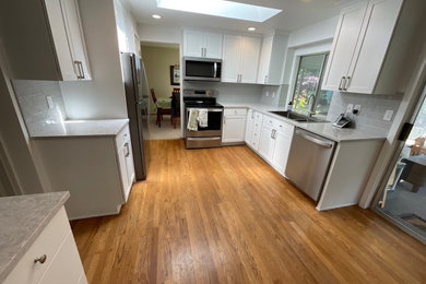 Example of a small arts and crafts l-shaped light wood floor and brown floor eat-in kitchen design in Seattle with a farmhouse sink, shaker cabinets, white cabinets, granite countertops, gray backsplash, ceramic backsplash, stainless steel appliances, no island and gray countertops