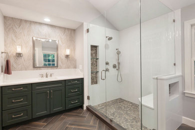 Photo of a large transitional master bathroom in Atlanta with recessed-panel cabinets, green cabinets, a freestanding tub, an alcove shower, a two-piece toilet, porcelain tile, grey walls, ceramic floors, an undermount sink, engineered quartz benchtops, brown floor, a hinged shower door, multi-coloured benchtops, a shower seat, a double vanity, a built-in vanity, vaulted and wallpaper.