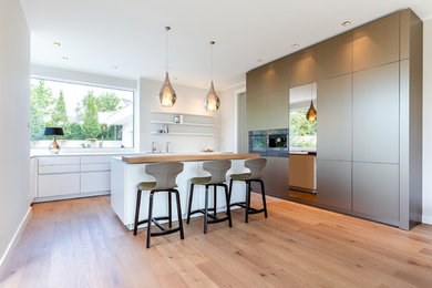 Offene, Große Moderne Küche in L-Form mit flächenbündigen Schrankfronten, Edelstahlfronten, Mineralwerkstoff-Arbeitsplatte, Küchenrückwand in Beige, Küchengeräten aus Edelstahl, braunem Holzboden, Kücheninsel und weißer Arbeitsplatte in Frankfurt am Main
