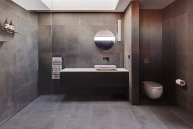 This is an example of a contemporary bathroom in Sydney with gray tile, grey walls, a vessel sink, furniture-like cabinets, dark wood cabinets, marble benchtops, an open shower, a wall-mount toilet and stone tile.