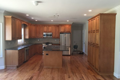 Inspiration for a huge timeless l-shaped medium tone wood floor open concept kitchen remodel in New York with a single-bowl sink, raised-panel cabinets, medium tone wood cabinets, granite countertops, beige backsplash, ceramic backsplash, stainless steel appliances and an island