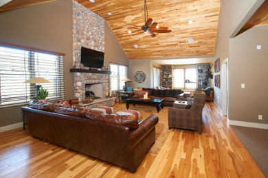 Example of an arts and crafts open concept medium tone wood floor family room design in Indianapolis with beige walls, a standard fireplace, a stone fireplace and a wall-mounted tv