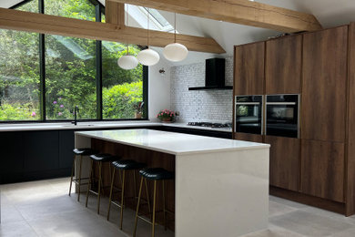 Inspiration for a medium sized contemporary l-shaped kitchen/diner in Hampshire with flat-panel cabinets, medium wood cabinets, granite worktops, grey splashback, ceramic splashback, black appliances, an island and white worktops.