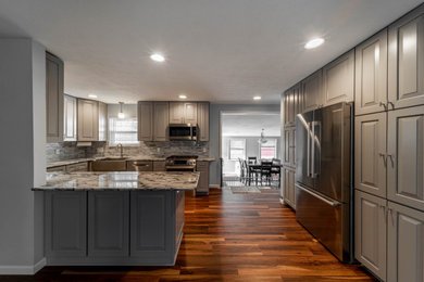 Example of a mid-sized classic u-shaped vinyl floor and brown floor eat-in kitchen design in Cleveland with a farmhouse sink, raised-panel cabinets, gray cabinets, granite countertops, gray backsplash, mosaic tile backsplash, stainless steel appliances, a peninsula and white countertops