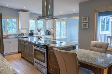 Inspiration for a large transitional u-shaped open plan kitchen in Toronto with an undermount sink, recessed-panel cabinets, white cabinets, granite benchtops, stainless steel appliances, light hardwood floors, with island, brown floor and grey benchtop.