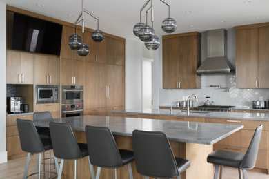 Photo of an expansive contemporary kitchen in Calgary with a submerged sink, dark wood cabinets, stainless steel appliances, light hardwood flooring, multiple islands and grey worktops.