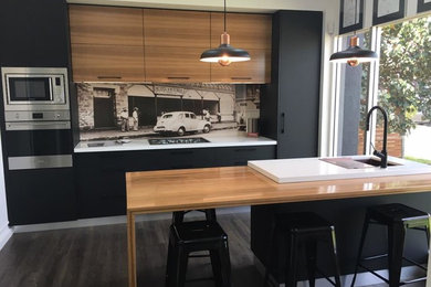 Mid-sized modern galley eat-in kitchen in Darwin with an undermount sink, black cabinets, wood benchtops, stainless steel appliances, laminate floors, with island and grey floor.