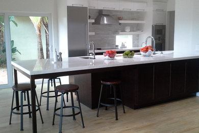 Open concept kitchen - mid-sized contemporary galley open concept kitchen idea in Miami with a single-bowl sink, flat-panel cabinets, white cabinets, quartz countertops, gray backsplash, stone tile backsplash, stainless steel appliances and a peninsula