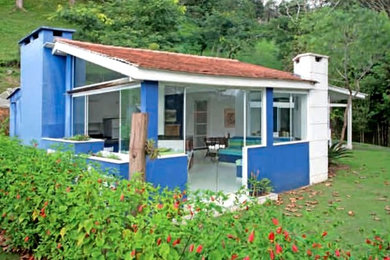 Small tropical blue one-story concrete exterior home idea in Other with a hip roof