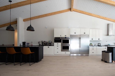 Eat-in kitchen - huge modern single-wall light wood floor, brown floor and vaulted ceiling eat-in kitchen idea in Montreal with an undermount sink, shaker cabinets, white cabinets, quartzite countertops, white backsplash, stainless steel appliances, two islands and black countertops