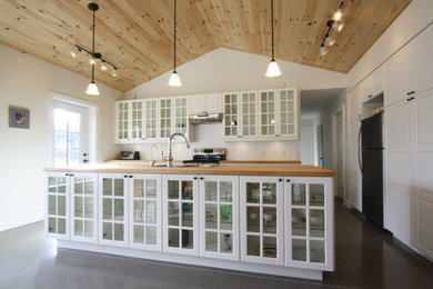 Mid-sized transitional galley concrete floor and brown floor open concept kitchen photo in Toronto with a double-bowl sink, glass-front cabinets, white cabinets, wood countertops, white backsplash, stainless steel appliances, an island and wood backsplash