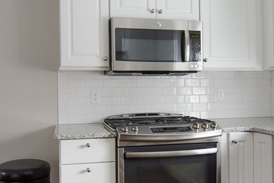 Elegant u-shaped eat-in kitchen photo in Boston with an integrated sink, raised-panel cabinets, white cabinets, granite countertops, white backsplash, subway tile backsplash and stainless steel appliances