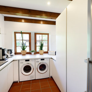 Design ideas for a small rural u-shaped utility room in Essen with a built-in sink, flat-panel cabinets, white cabinets, white walls, terracotta flooring, a side by side washer and dryer, red floors and white worktops.