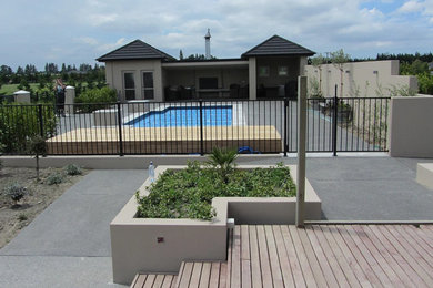 This is an example of a large contemporary backyard custom-shaped aboveground pool in Christchurch with a pool house and concrete pavers.