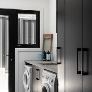 ホバートのコンテンポラリースタイルのおしゃれな洗濯室 (フラットパネル扉のキャビネット、黒いキャビネット、白い壁、左右配置の洗濯機・乾燥機、グレーの床、グレーのキッチンカウンター) の写真
