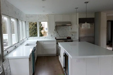Inspiration for a mid-sized transitional l-shaped medium tone wood floor and brown floor kitchen remodel in New York with a farmhouse sink, shaker cabinets, white cabinets, quartzite countertops, white backsplash, marble backsplash, stainless steel appliances and an island