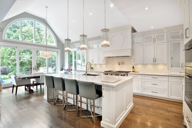 Photo of a large transitional l-shaped kitchen pantry in Toronto with an undermount sink, shaker cabinets, white cabinets, quartz benchtops, white splashback, marble splashback, panelled appliances, medium hardwood floors, with island, brown floor and white benchtop.
