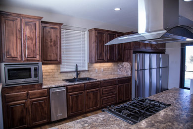 Mid-sized elegant galley medium tone wood floor open concept kitchen photo in Dallas with a double-bowl sink, raised-panel cabinets, dark wood cabinets, laminate countertops, beige backsplash, stone tile backsplash and stainless steel appliances