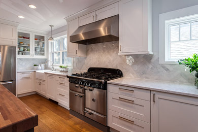 Large farmhouse u-shaped medium tone wood floor and brown floor open concept kitchen photo in Denver with a farmhouse sink, shaker cabinets, white cabinets, marble countertops, white backsplash, stone slab backsplash, stainless steel appliances and an island