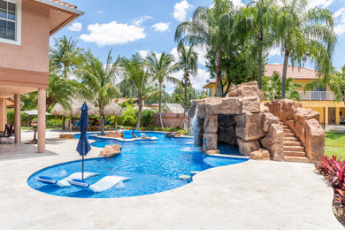 Inspiration for an expansive tropical backyard custom-shaped natural pool in Miami with a water slide and natural stone pavers.