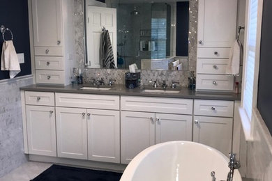 This is an example of a mid-sized transitional master bathroom in New York with shaker cabinets, white cabinets, a freestanding tub, gray tile, ceramic tile, purple walls, ceramic floors, an undermount sink, engineered quartz benchtops, white floor and grey benchtops.