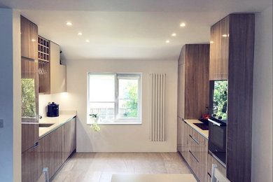Design ideas for a medium sized modern galley open plan kitchen in London with flat-panel cabinets, dark wood cabinets, quartz worktops, black appliances, ceramic flooring, no island, grey floors and white worktops.