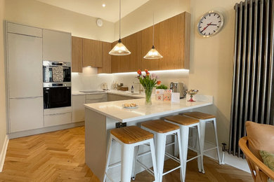 Medium sized modern u-shaped kitchen/diner in Other with a single-bowl sink, flat-panel cabinets, medium wood cabinets, quartz worktops, white splashback, black appliances, medium hardwood flooring, no island, brown floors, white worktops and a coffered ceiling.