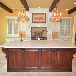 Large traditional kitchen pantry inspiration - Example of a large classic l-shaped travertine floor kitchen pantry design in Louisville with an undermount sink, glass-front cabinets, white cabinets, quartzite countertops, beige backsplash, stone tile backsplash, stainless steel appliances and an island