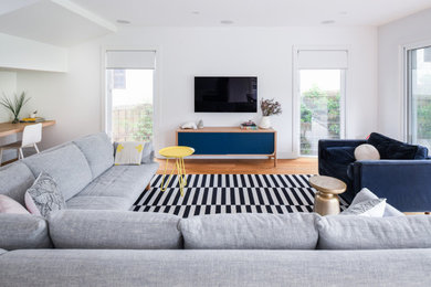 Ejemplo de sala de estar abierta contemporánea con paredes blancas, suelo de madera en tonos medios y televisor colgado en la pared