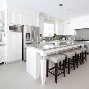 Idee per una cucina a L tradizionale di medie dimensioni con lavello sottopiano, ante in stile shaker, ante bianche, top in granito, paraspruzzi grigio, paraspruzzi con piastrelle di vetro, elettrodomestici in acciaio inossidabile, pavimento in gres porcellanato e isola