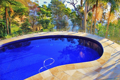 Photo of a contemporary backyard custom-shaped pool in Sydney with natural stone pavers.