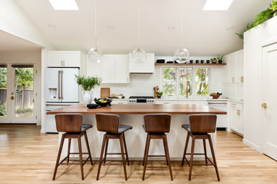 Inspiration for a mid-sized scandinavian l-shaped light wood floor and vaulted ceiling eat-in kitchen remodel in Seattle with an undermount sink, recessed-panel cabinets, white cabinets, quartz countertops, white backsplash, subway tile backsplash, white appliances, an island and white countertops