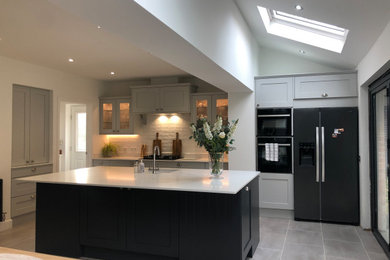 Design ideas for a large traditional galley open plan kitchen in Glasgow with an integrated sink, shaker cabinets, grey cabinets, quartzite benchtops, white splashback, ceramic splashback, black appliances, porcelain floors, with island, grey floor and white benchtop.