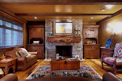 Family room - large rustic enclosed medium tone wood floor and brown floor family room idea in Calgary with brown walls, a standard fireplace, a stone fireplace and no tv