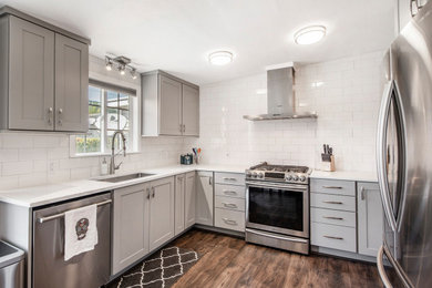 Example of a mid-sized transitional u-shaped laminate floor and brown floor eat-in kitchen design in Salt Lake City with an undermount sink, shaker cabinets, gray cabinets, quartz countertops, white backsplash, ceramic backsplash, stainless steel appliances and white countertops