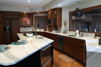 Example of a large classic u-shaped medium tone wood floor and brown floor enclosed kitchen design with an undermount sink, raised-panel cabinets, medium tone wood cabinets, marble countertops, gray backsplash, matchstick tile backsplash, stainless steel appliances and an island