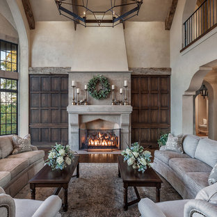 Imagen de salón abierto, mediterráneo, grande, con paredes beige, suelo de madera en tonos medios, marco de chimenea de piedra, chimenea tradicional, televisor retractable y suelo beige