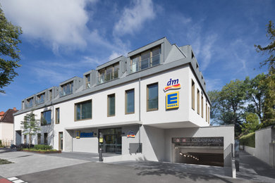 This is an example of a mid-sized contemporary three-storey stucco white exterior in Munich with a clipped gable roof, a green roof and a grey roof.