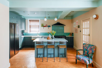 Design ideas for a medium sized contemporary l-shaped kitchen/diner in Kent with a belfast sink, recessed-panel cabinets, green cabinets, laminate countertops, green splashback, ceramic splashback, black appliances, cork flooring, an island, beige floors, green worktops, exposed beams and feature lighting.