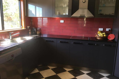 Klassisk inredning av ett avskilt, mellanstort u-kök, med en dubbel diskho, grå skåp, bänkskiva i kvarts, rött stänkskydd, stänkskydd i keramik, rostfria vitvaror, linoleumgolv och flerfärgat golv
