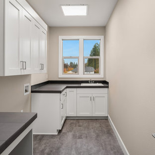 ポートランドの中サイズのトランジショナルスタイルのおしゃれな洗濯室 (ドロップインシンク、落し込みパネル扉のキャビネット、白いキャビネット、タイルカウンター、グレーの壁、クッションフロア、左右配置の洗濯機・乾燥機、グレーの床、黒いキッチンカウンター) の写真