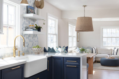 This is an example of a beach style kitchen in San Diego with a farmhouse sink, quartz benchtops, blue splashback, glass tile splashback, light hardwood floors, a peninsula and white benchtop.